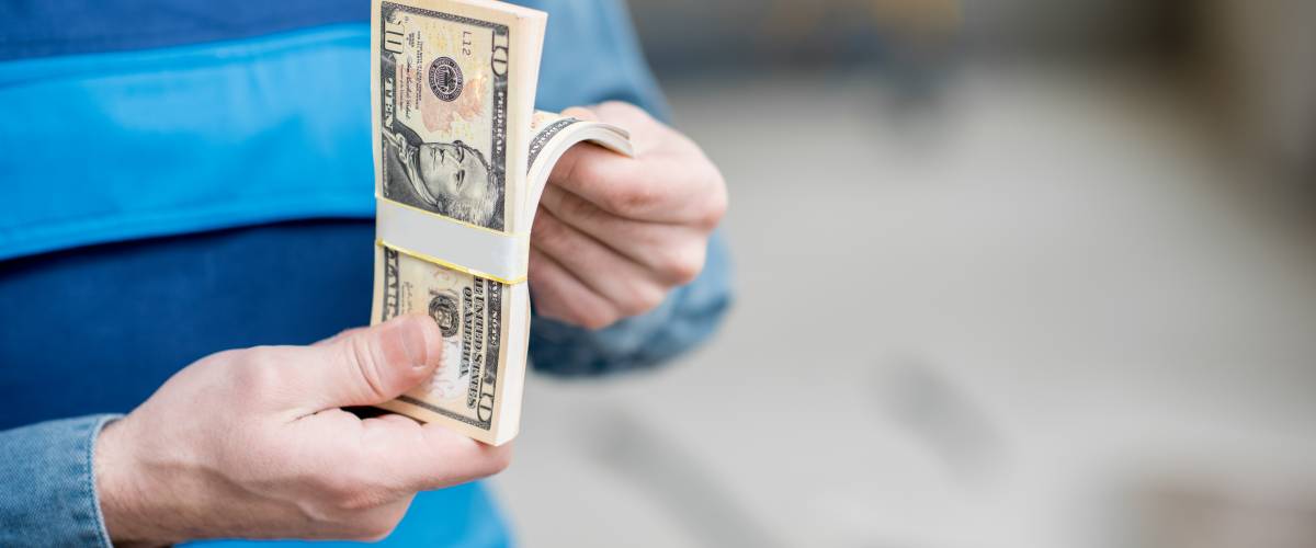 Man in a striped shirt counts pile of cash, close up of hands holding money.