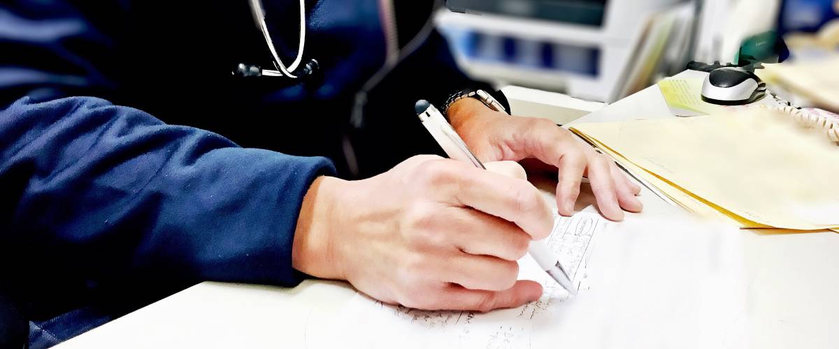 Close up of doctor wearing a stethoscope, writing on a medical pad.