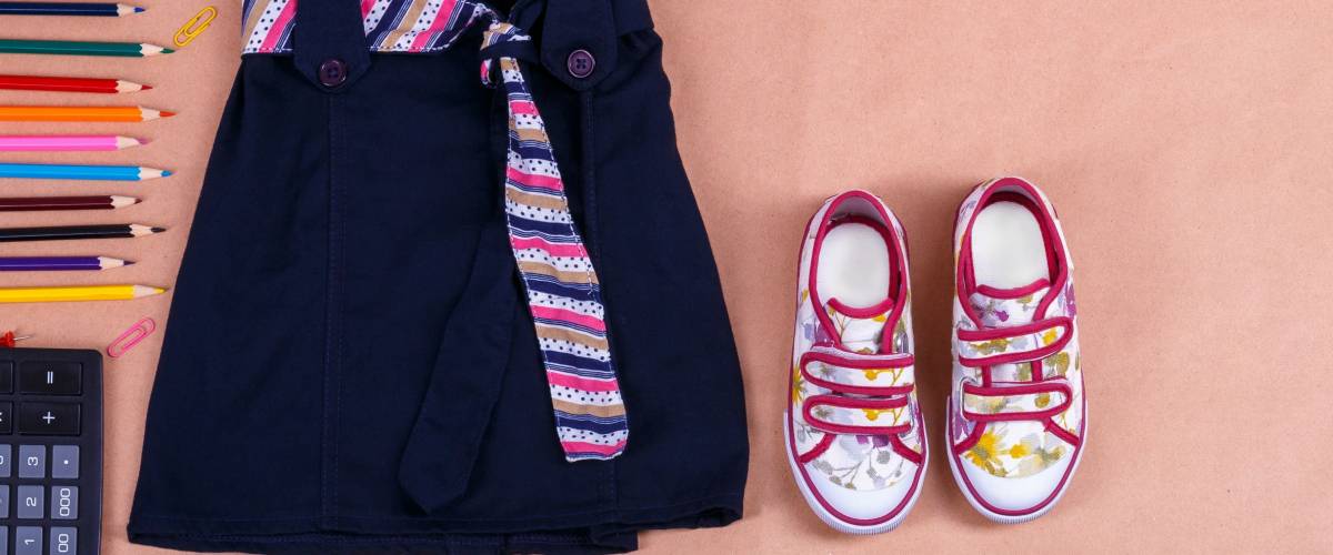 School uniform near sneakers and school supplies on orange background with an inscription school. Top view, Copy space. outfit. Back to school.