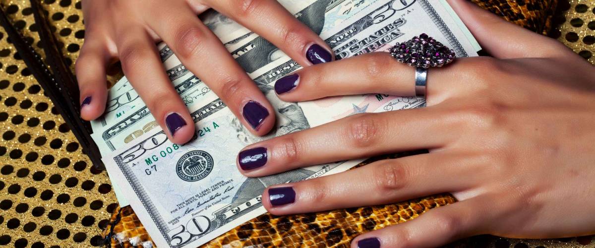 pretty fingers of african american woman holding money closeup with purse, luxury jewellery on python clutch, cash for gifts