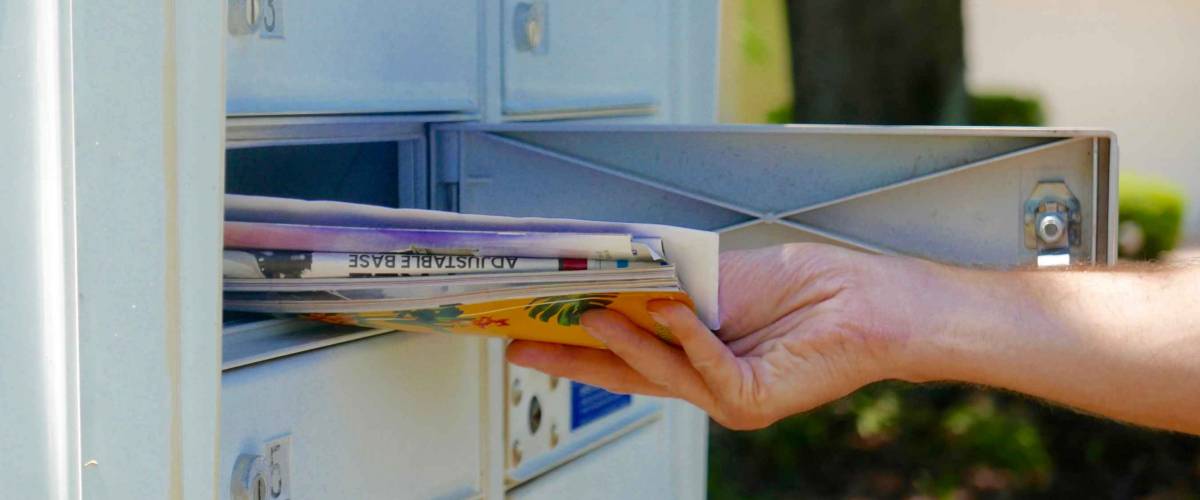 Person's hand pulling a pile of mail out of an outdoor community mailbox