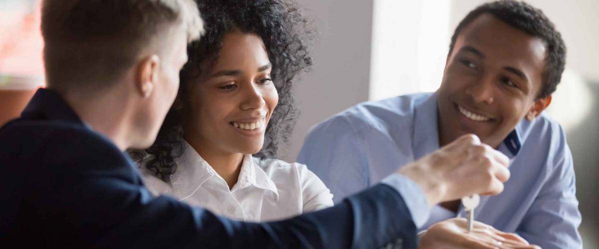 Man handing over key to smiling couple, woman holding out her hand.