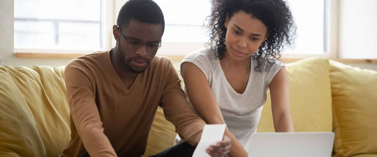 Serious african american couple using calculator and laptop for calaulating finance. Diverse upset man and woman taxing, accounting with check credit analytic for mortgage payment.