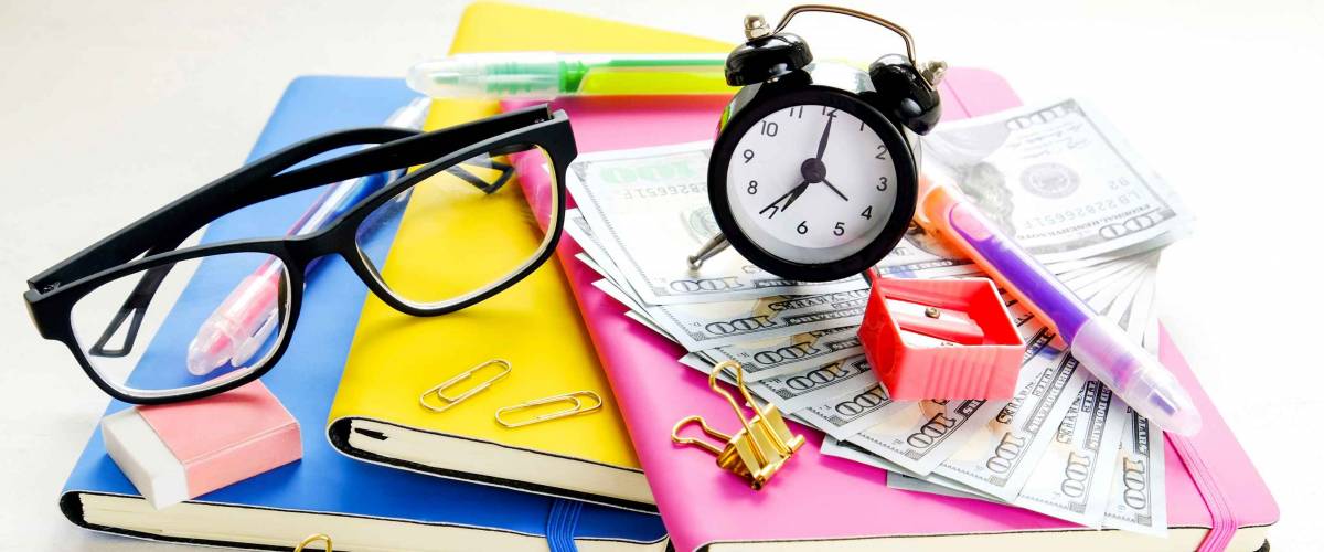Investing time & money in expensive education, college tuition & fees concept. Pack of new one hundred dollar bills, notebooks, school supplies, alarm clock.