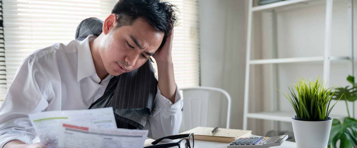 Stressed young asian businessman holding so many expenses bills such as electricity bill,water bill,internet bill,cell phone bill and credit card bill in his hand no money to pay debt