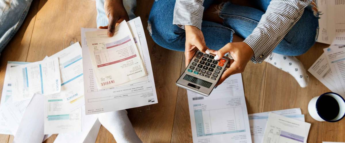 Couple seen from above looking t piles of bills, holding a calculator.