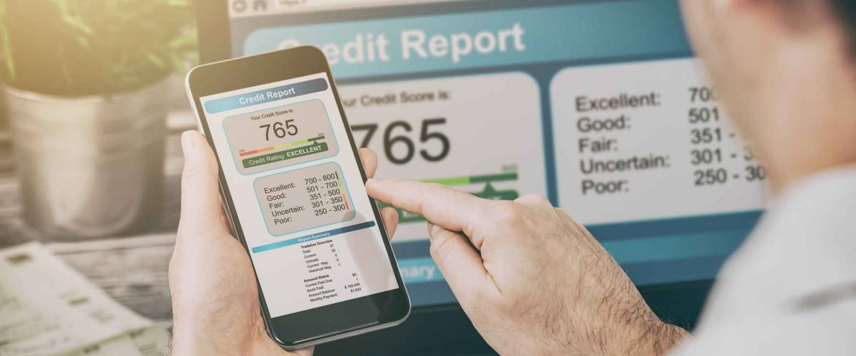 Man looking at credit score report on both phone and laptop screen.
