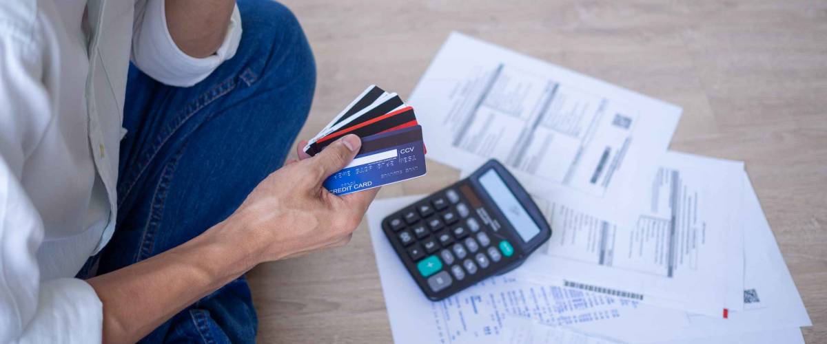 Man sitting on the ground with a pile of bills fanned out, holding onto a few credit cards.