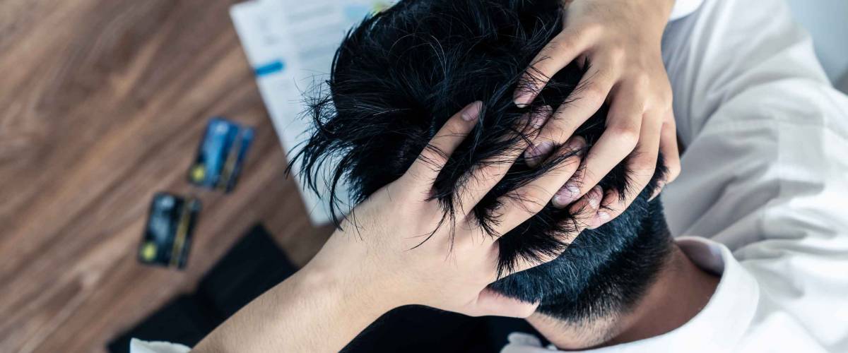 Top view of stressed young Asian man sitting and hugging knees, trying to find money to pay credit card debt and all loan bills.