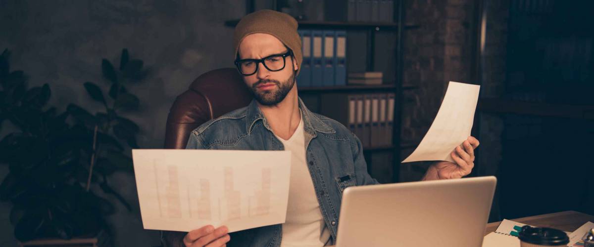 Photo of attentive guy work at dark day time reading finance income papers wear casual outfit sit modern office