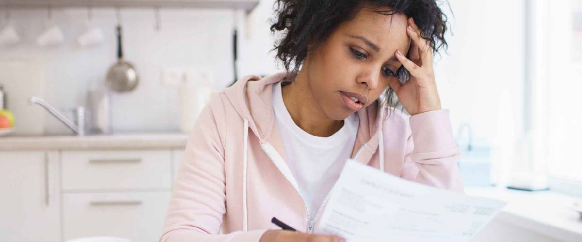 Upset african american female sitting at kitchen table with laptop, dealing with financial stress and pressure because of mortgage debt, worrying a lot or feeling anxious over money