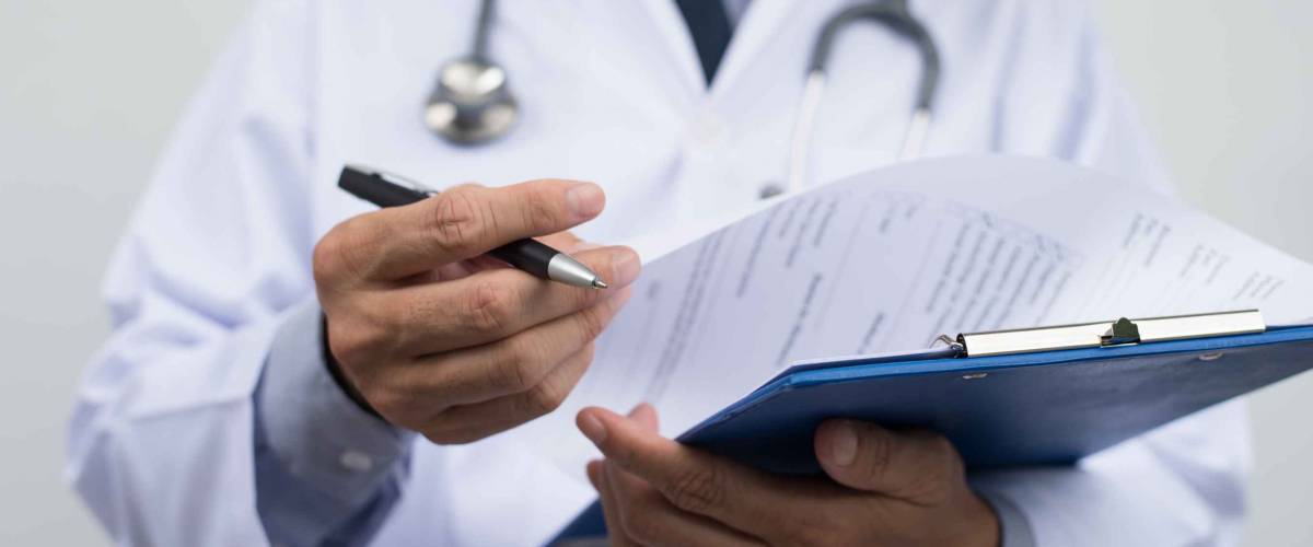 Male doctor on duty in white coat reading patient's information with pen in hand.