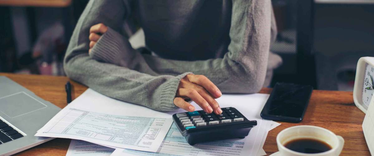 Close up of woman using a calculator while sitting at a desk.