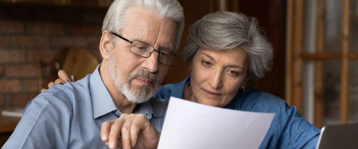 Older couple looking closely at a piece of paper, look interested.