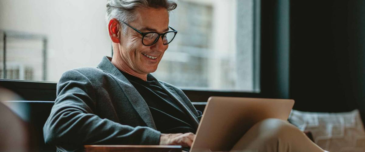 Smiling businessman looking at laptop, sitting on a couch.