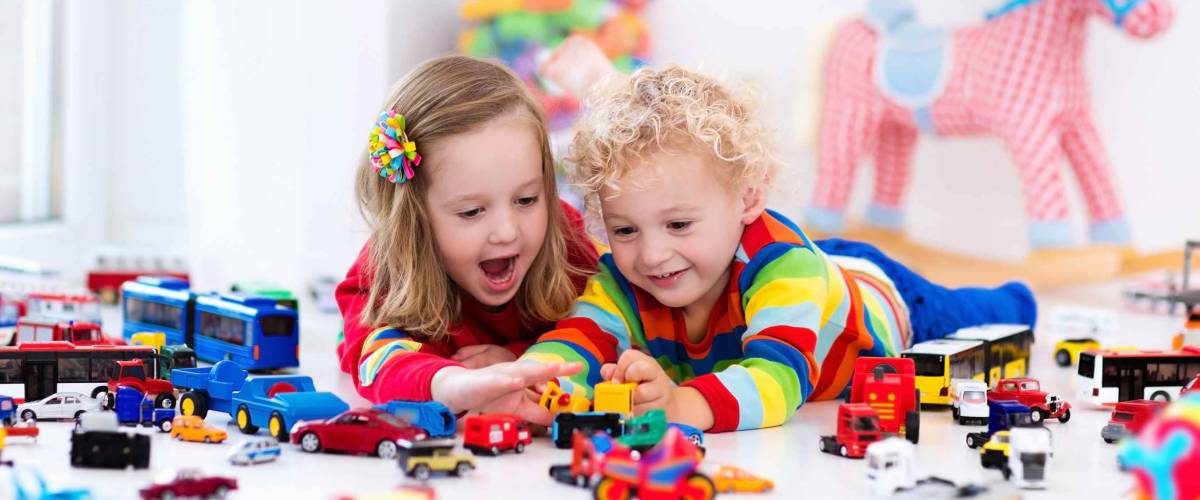 Little toddler boy and girl playing with model car collection on the floor.