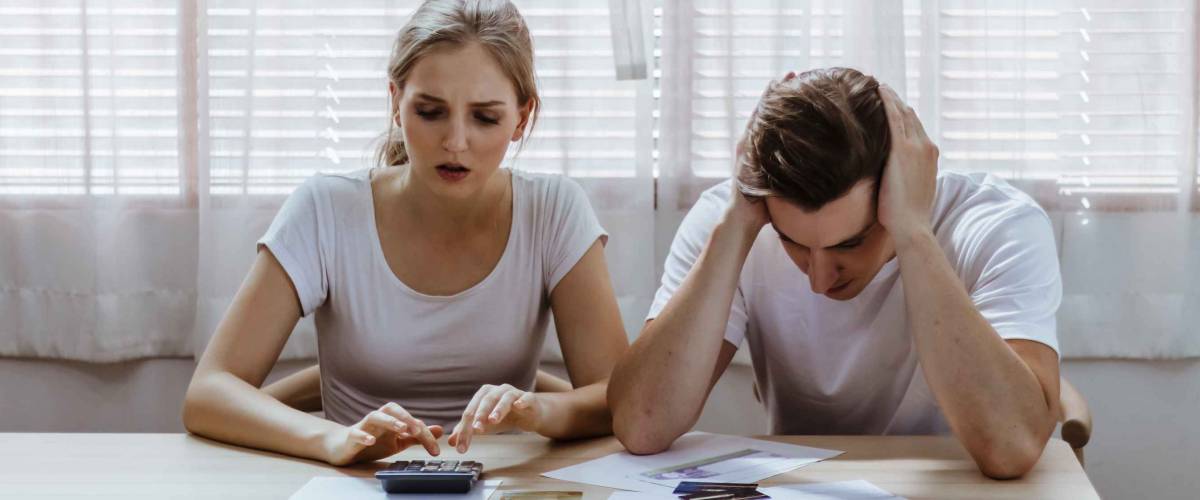 Stressed young couple look at bills at kitchen table.