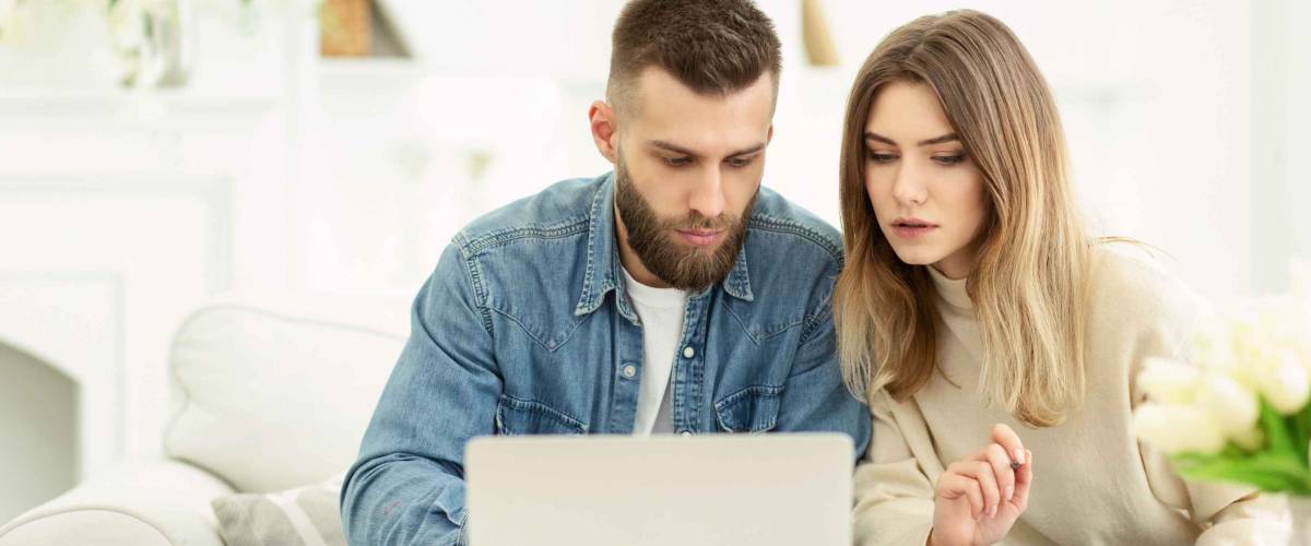 Millennial couple managing expenses with laptop and checking accountancy and bills, panorama