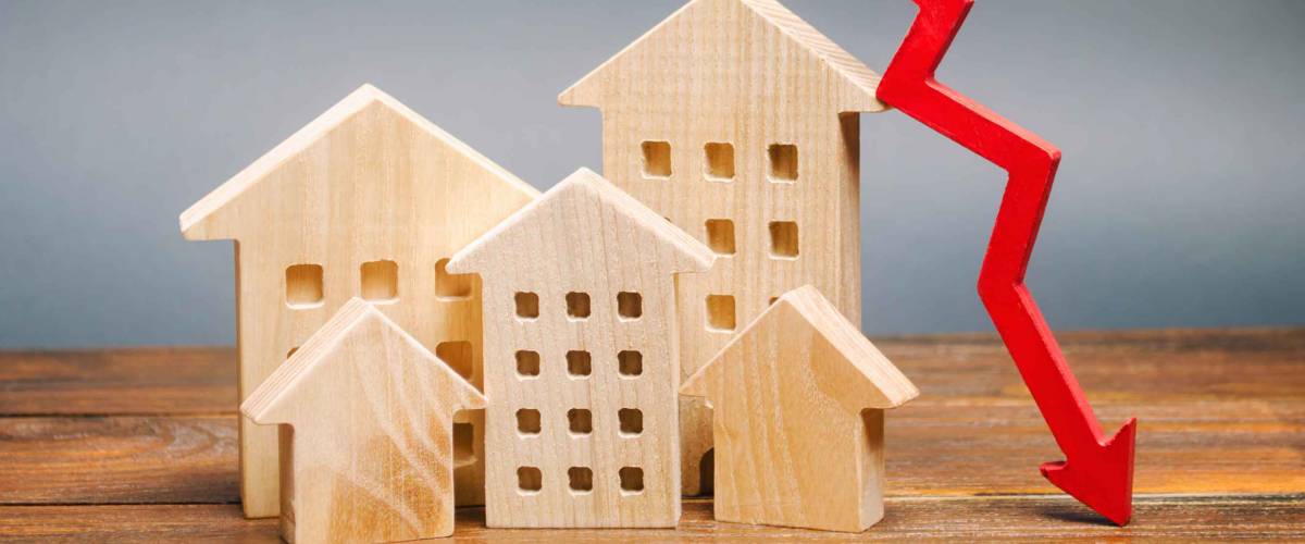 Miniature wooden houses and a red arrow down. The concept of lower mortgage interest rates.