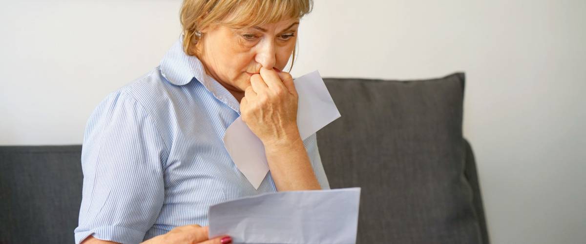 An elderly woman reads negative news in a letter at home on the couch. An elderly woman received a notice of the loss of a child, her husband.