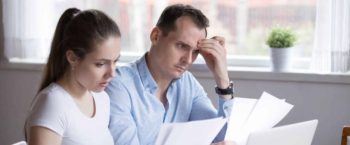Serious looking couple looking at pieces of papers while sitting at table.