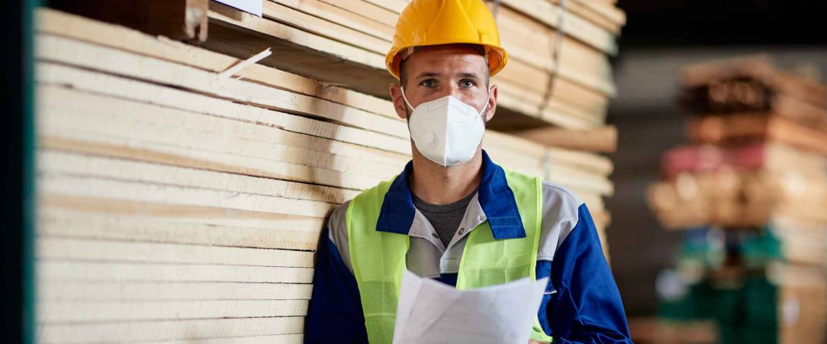 Portrait of warehouse worker in timber storage compartment wearing face mask due to coronavirus pandemic.