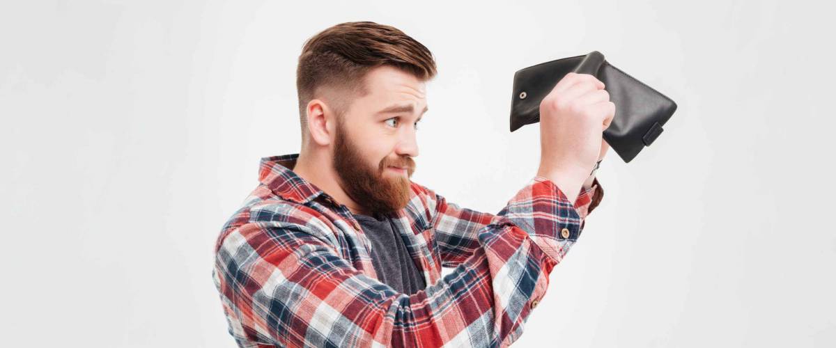 Young bearded man in plaid shirt looking inside his empty wallet to camera over white background over white background