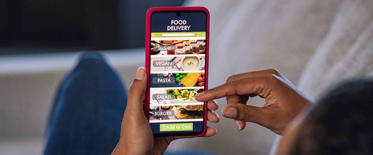 Woman lying on couch using food delivery app on smartphone. Close up of african woman hands holding cellphone and ordering food online.