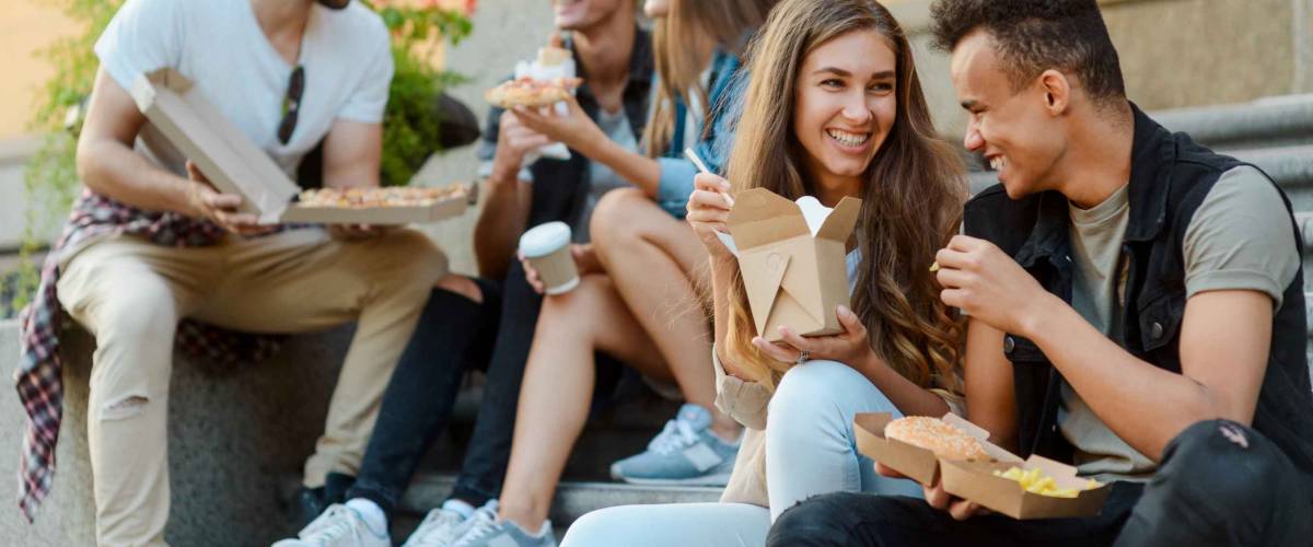 Five friends are dining together outdoors. Wok noodles, hamburger, frites and pizza. Eating street food concept.
