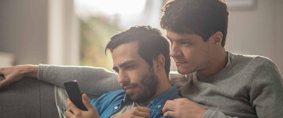 Two men sitting on a couch, looking seriously at a smartphone.