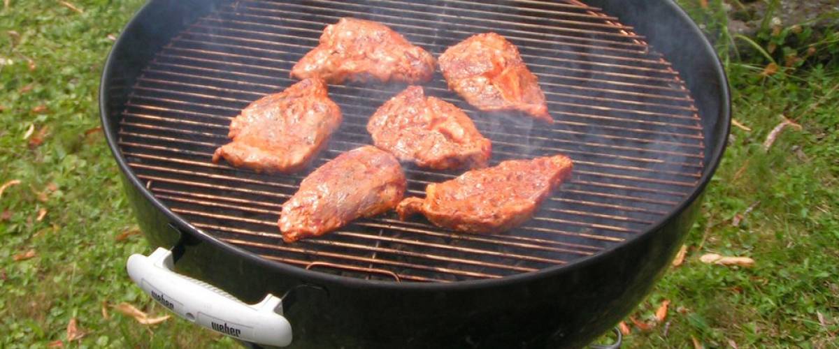 Weber barbecue with meat on it, grilling.
