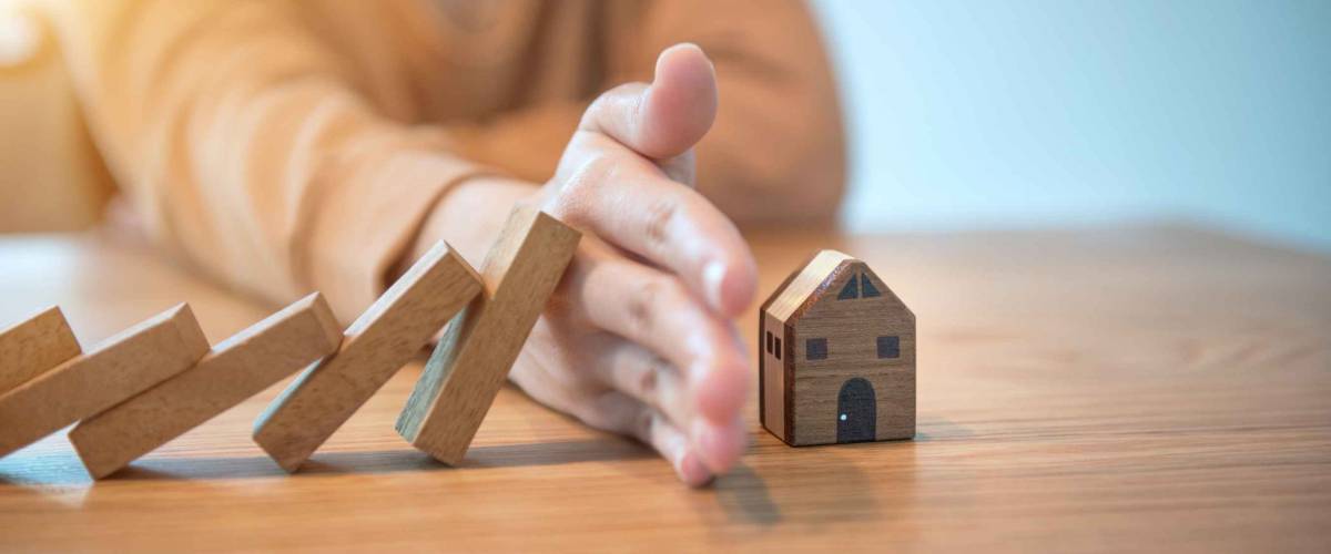 Woman hand stopping risk the wooden blocks from falling on house,