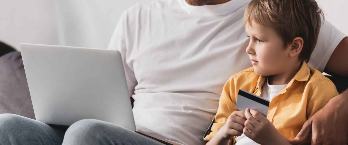 concentrated father using laptop while adorable son holding credit card