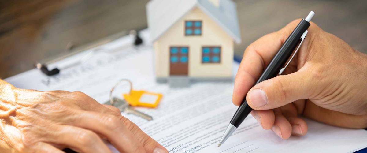 Close-up Of A Real Estate Agent's Hand Helping Client In Filling Contract Form Over Desk