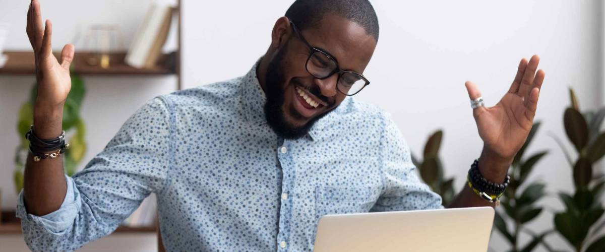 Joyful black businessman sitting at desk looking at computer screen