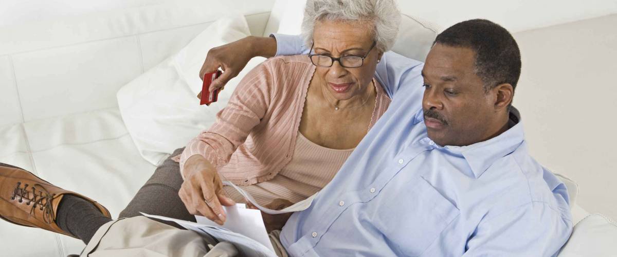 High angle view of senior African American couple looking at bills while sitting on sofa