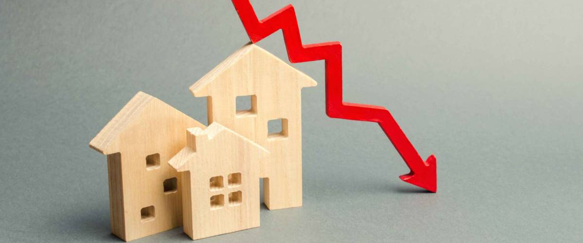 Miniature wooden houses and a red arrow down. The concept of lower mortgage interest rates.
