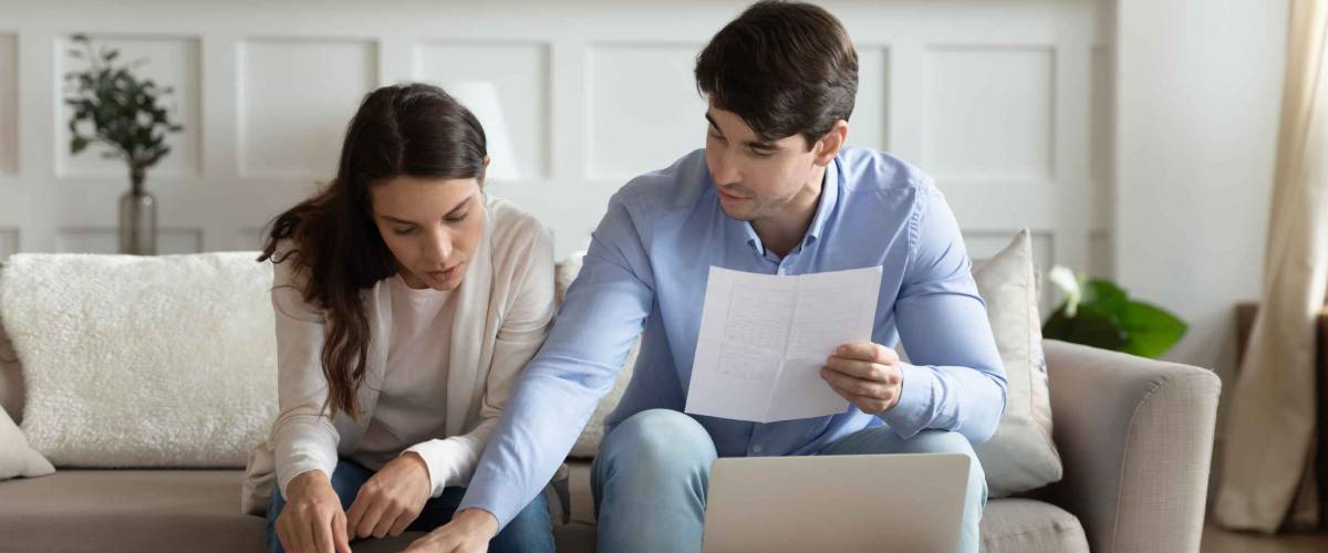 Payday. Concentrated attentive millennial spouses sitting on couch at home discussing mortgage possibilities.