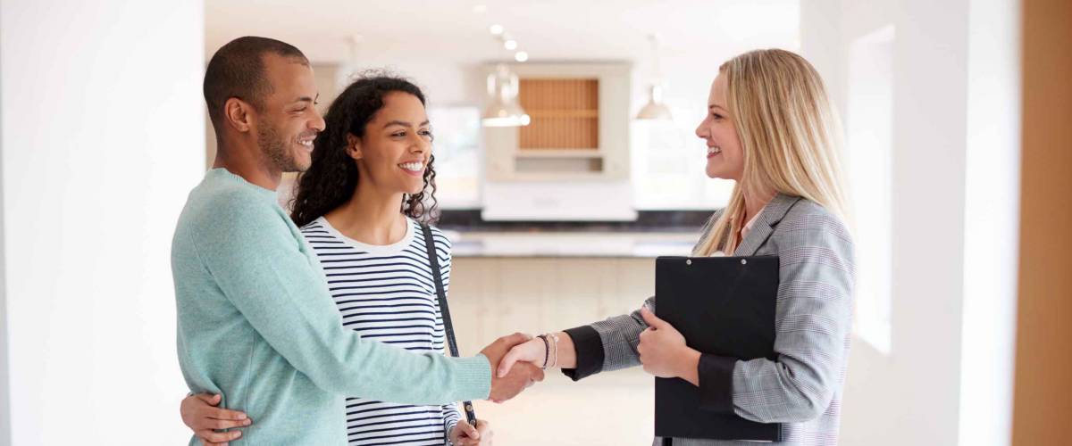 Female Realtor Shaking Hands With Couple Interested In Buying House