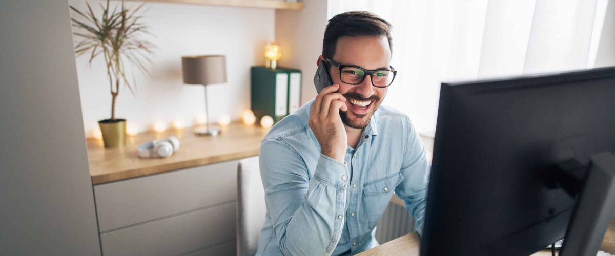 Smiling handsome freelancer working remotely, talking on the phone.