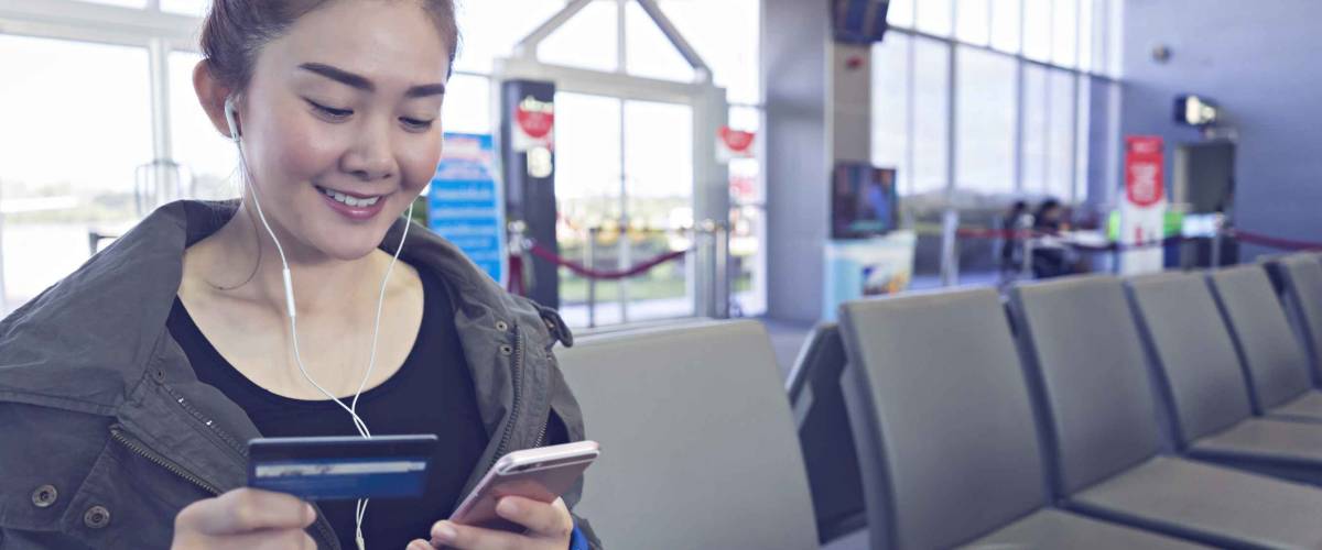 Shot of aisian women holding a credit card and purchasing online. young women paying with credit card on smart phone at airport.