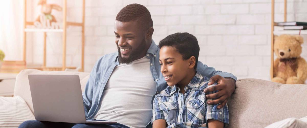 Cheerful Father And Son Watching Laptop Together, Relaxing On Couch At Home.