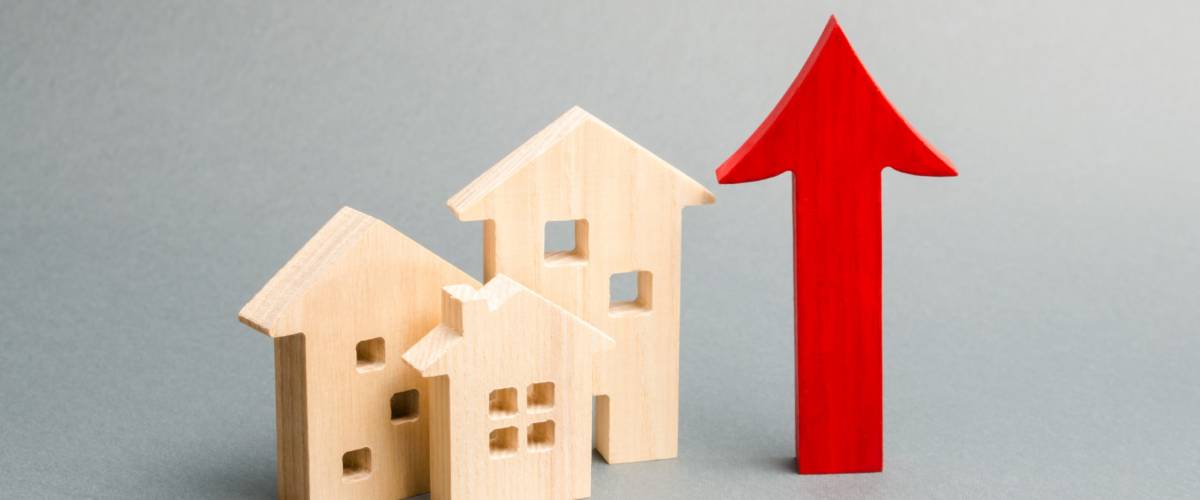 Miniature wooden houses and red arrow up. The concept of rising mortgage rates.