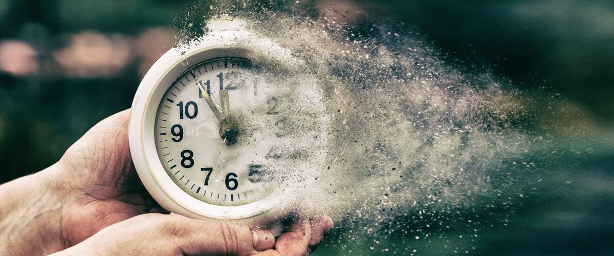 Retro alarm clock or vintage alarm clock in old hand. Time is running out concept shows clock that is dissolving away into little particles