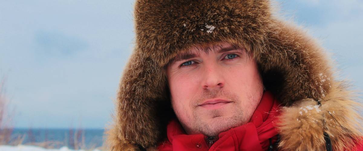 A young man in a winter red jacket looks straight ahead seriously. Winter portrait of a young man
