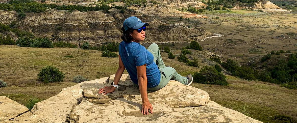A woman on sitting on the cliff with badlands on the background.