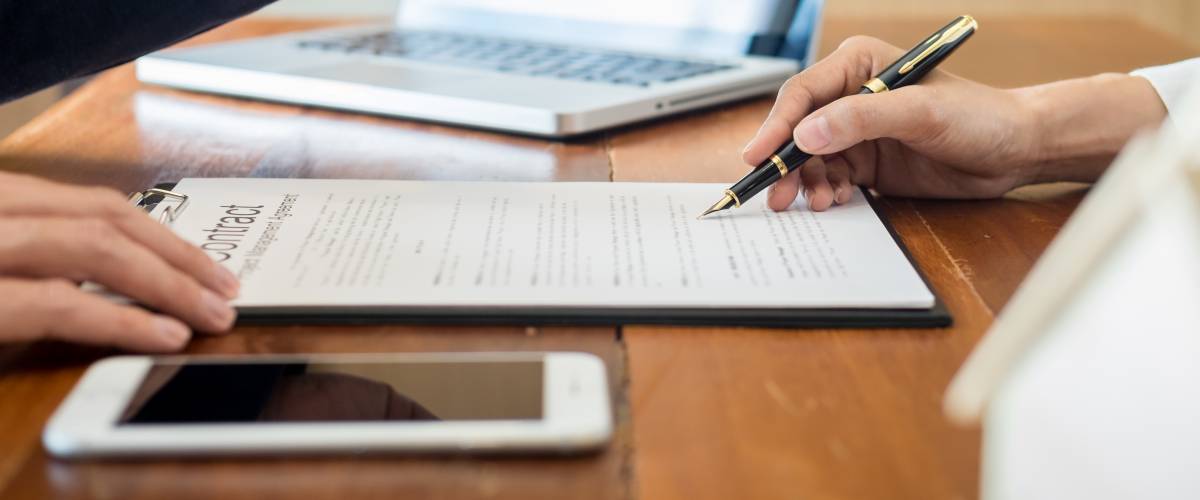Close up of person signing contract on a desk.