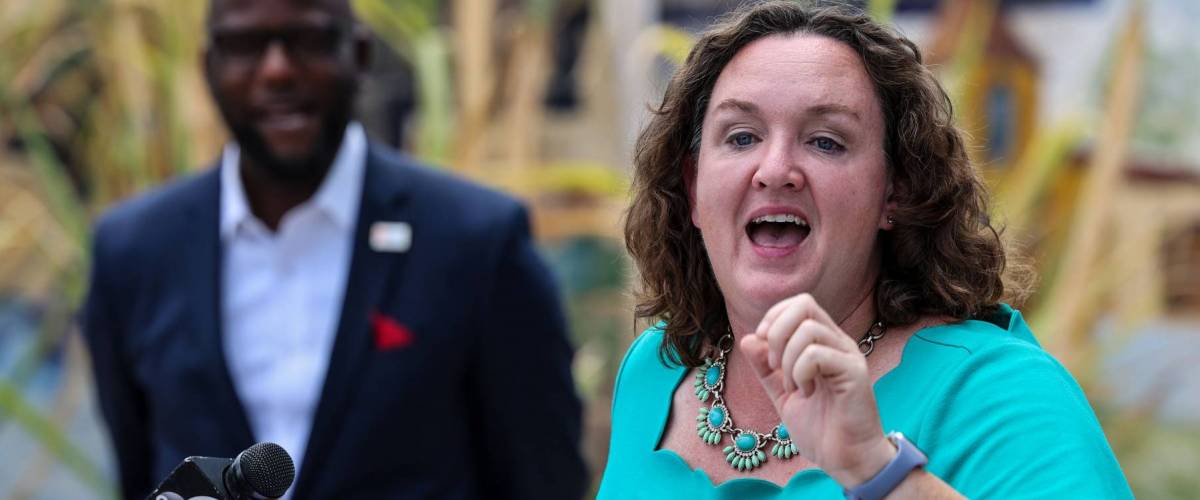 Rep. Katie Porter stands at a podium outside, talking with her hand gesturing.