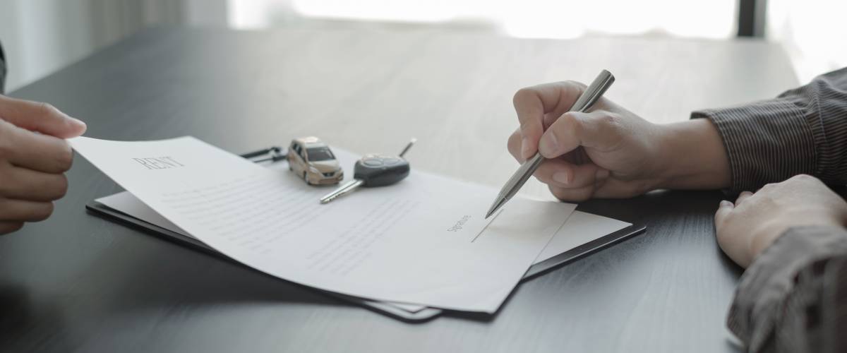 Close up of person signing piece of paper with keys and little toy car on it.