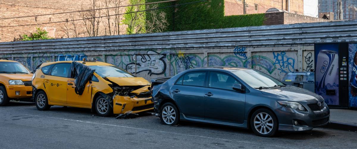Row of cars at the side of the road in front of a graffiti wall.